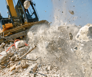 Excavator grapples crushing concrete block in air