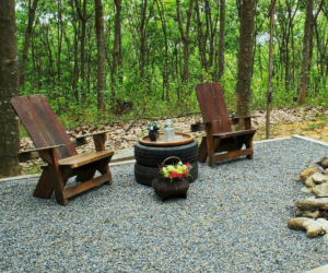 Two rock fire pit with wood table and chairs on gravel floor in the garden@1x