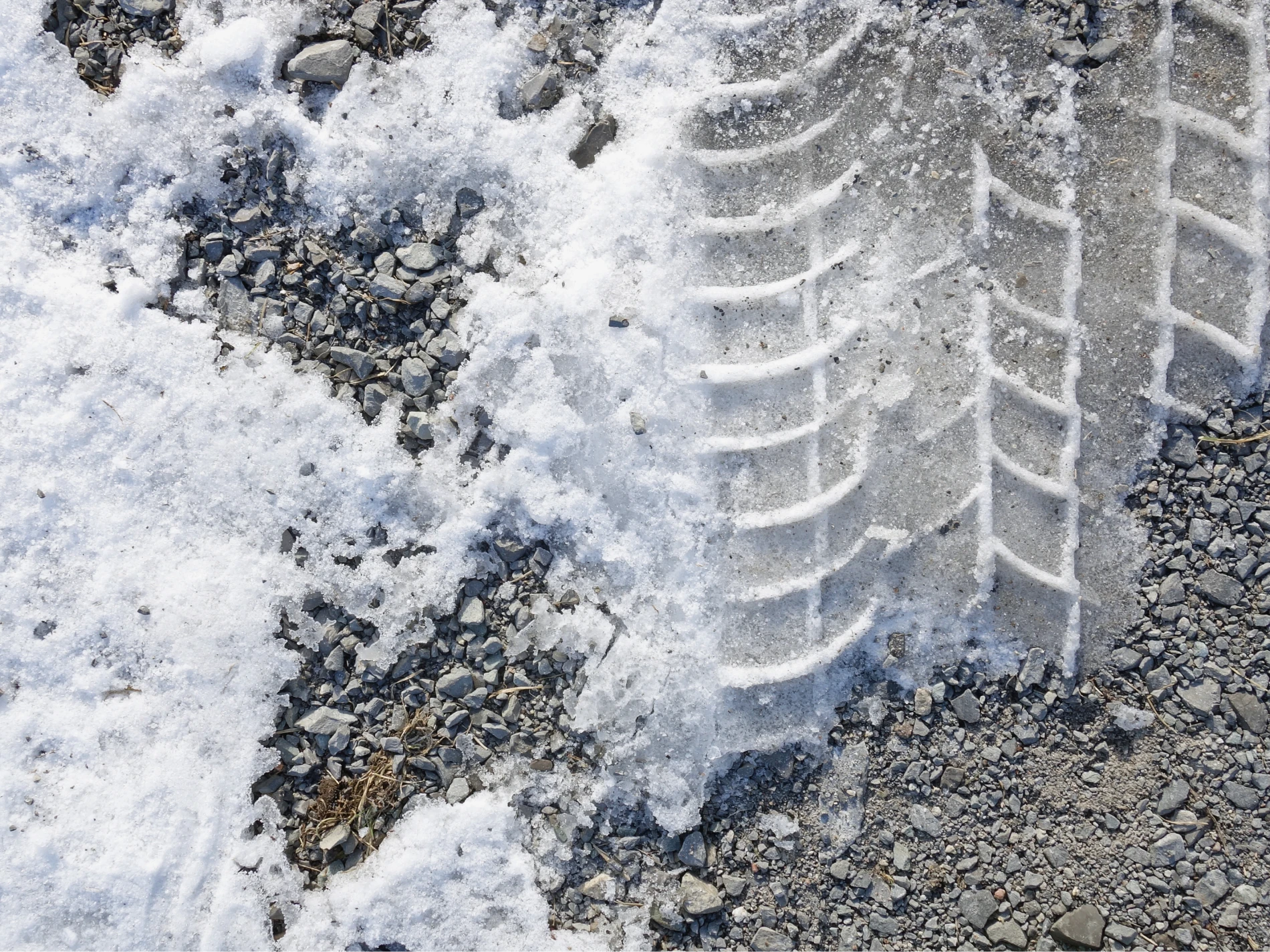 Snow covered tire tracks on a gravel driveway