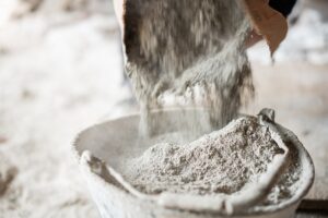 Close-up of a worker filling a bucket with sand and cement from a bag at construction site.