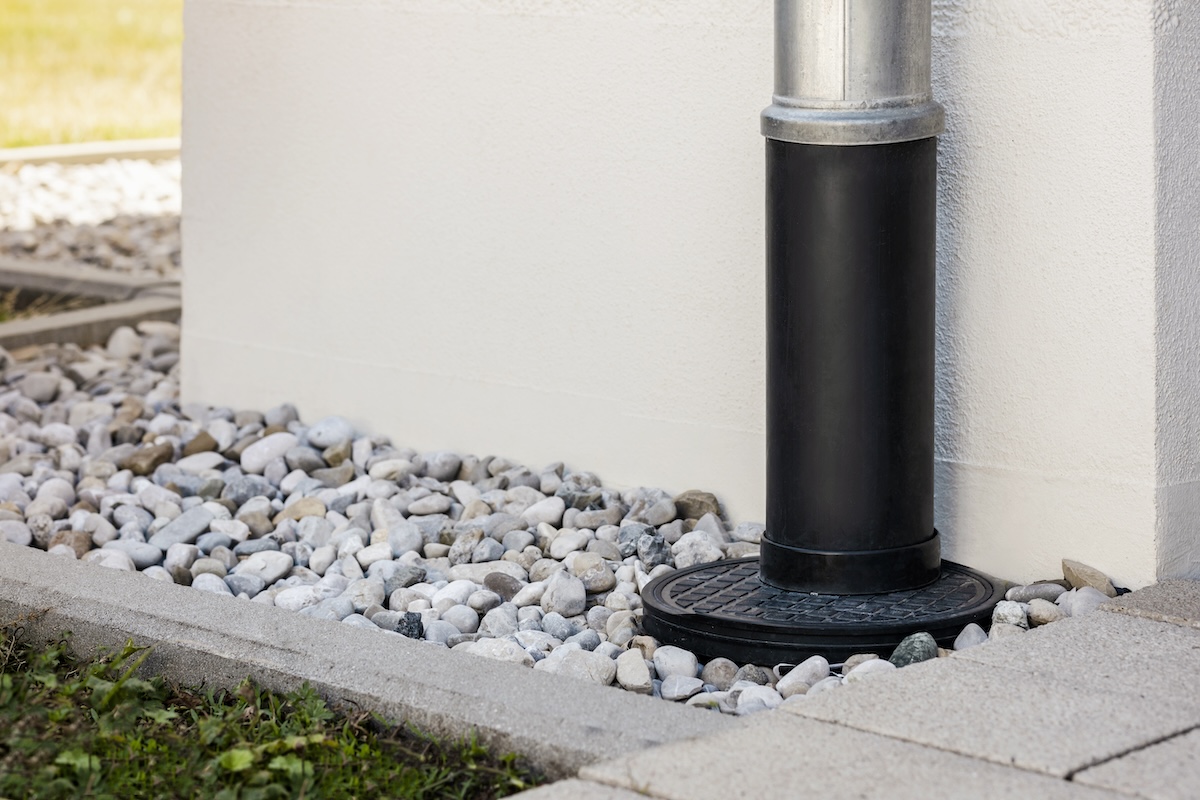 Downspout or Downpipe into French Drain Stones Floor Around Wall Building Outside. Modern Drainage System for Stormwater or Rainwater with Gravel Stones Covering by House Wall.