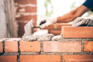 Bricklayer worker installing brick masonry on exterior wall with trowel putty knife with mortar sand